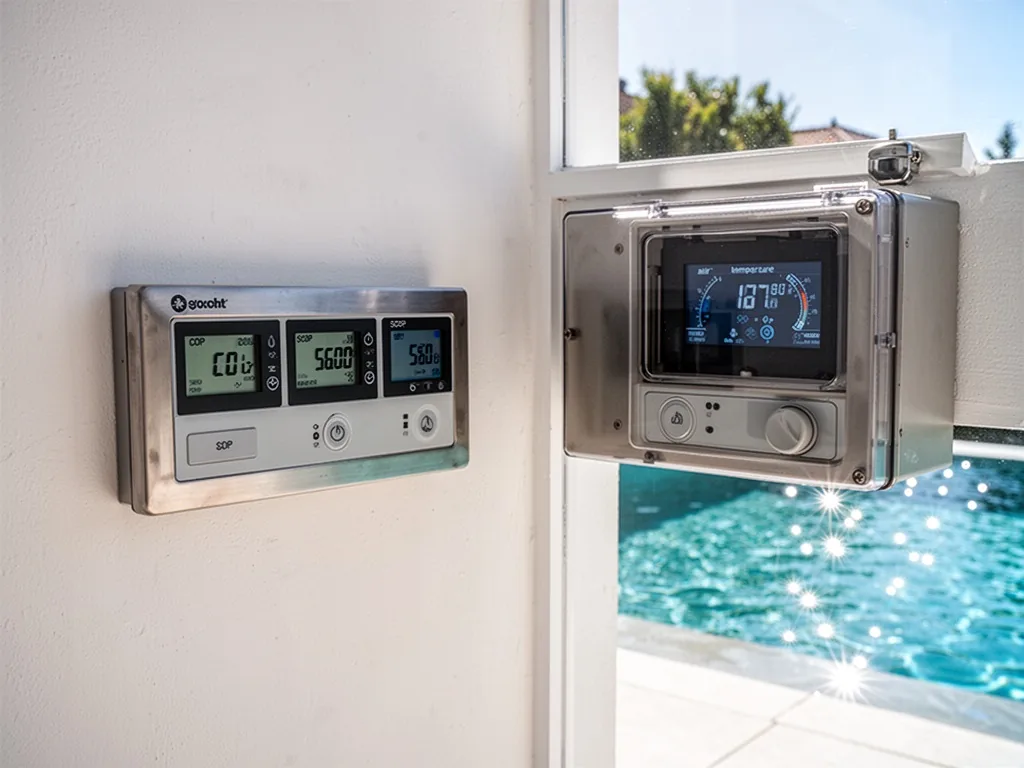 A pool heating control panel with three digital displays showing COP, SCOP and air temperature, mounted on a white wall